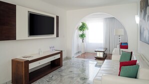En moderne stue med et fladskærms-tv, et træ-konsolbord, en hvid sofa med farverige puder og et stort vindue med gardiner.