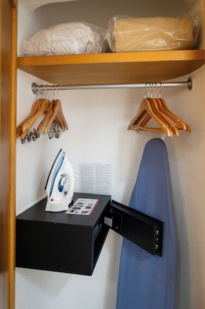 Ein Kleiderschrank mit Kleidung, einem Bügelbrett und einem Bügeleisen.