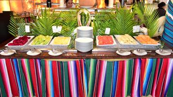 A buffet with various food options, including fruits and vegetables, and a colorful striped tablecloth.