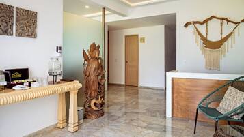 A reception area with a wooden reception desk, a decorative wooden sculpture, a hammock, and a wicker chair.