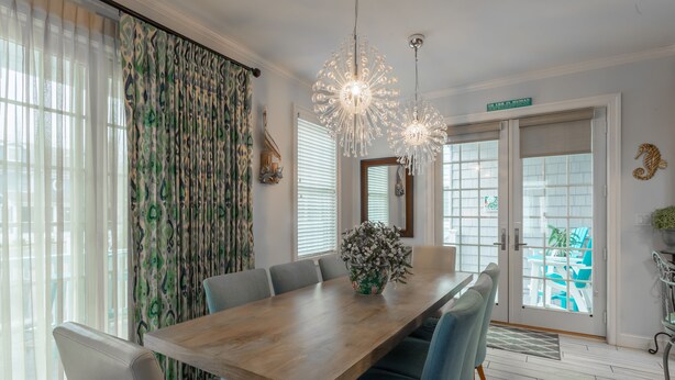 A dining area with a wooden table, blue upholstered chairs, a floral centerpiece, and a chandelier.