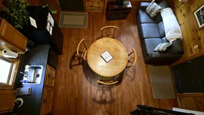 A compact cabin-style room with a round wooden dining table, a sofa, and a kitchenette.