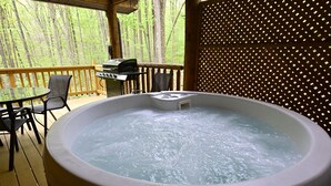 A hot tub on a wooden deck with a view of a forest.