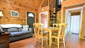 A cozy wooden cabin interior with a sofa, a dining table with chairs, and a staircase.