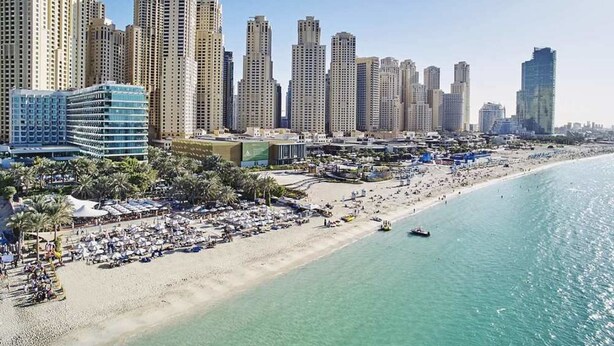 Paesaggio costiero con edifici alti, una spiaggia sabbiosa e numerosi ombrelloni.
