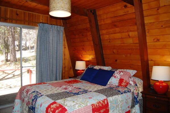 A cozy bedroom with a wooden ceiling, a large bed with a floral quilt, two bedside lamps, and a window with curtains.