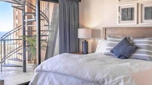 Een slaapkamer met een bed, een nachtkastje, een lamp en uitzicht op een trap die naar een balkon leidt.