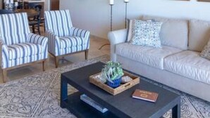 Een woonkamer met gestreepte fauteuils, een bank, een salontafel met decoratieve objecten, en een plafondventilator.