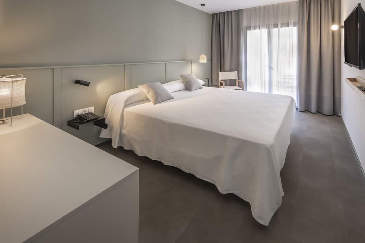 Een moderne hotelkamer met een groot bed, nachtkastjes, een televisie en een raam met gordijnen.