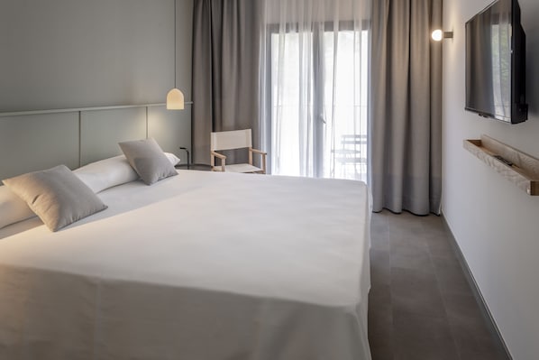 A modern hotel room with a large bed, a bedside table, a chair, a TV mounted on the wall, and a window with curtains. - GHT Miratge - Adults Only (Lloret de Mar)