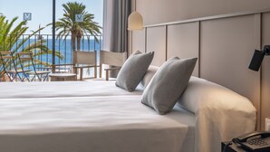 Ett hotellrum med en stor säng, ett skrivbord och utsikt över havet.