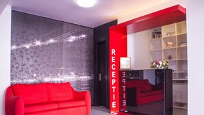 Un área de recepción moderna con un sofá rojo, un mural con vista a la ciudad y un mostrador de recepción con una pared de acento roja.