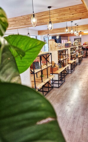 Un mercado interior amplio con estantes de madera repletos de diversos productos, lámparas colgantes y un techo a la vista con vigas de madera.