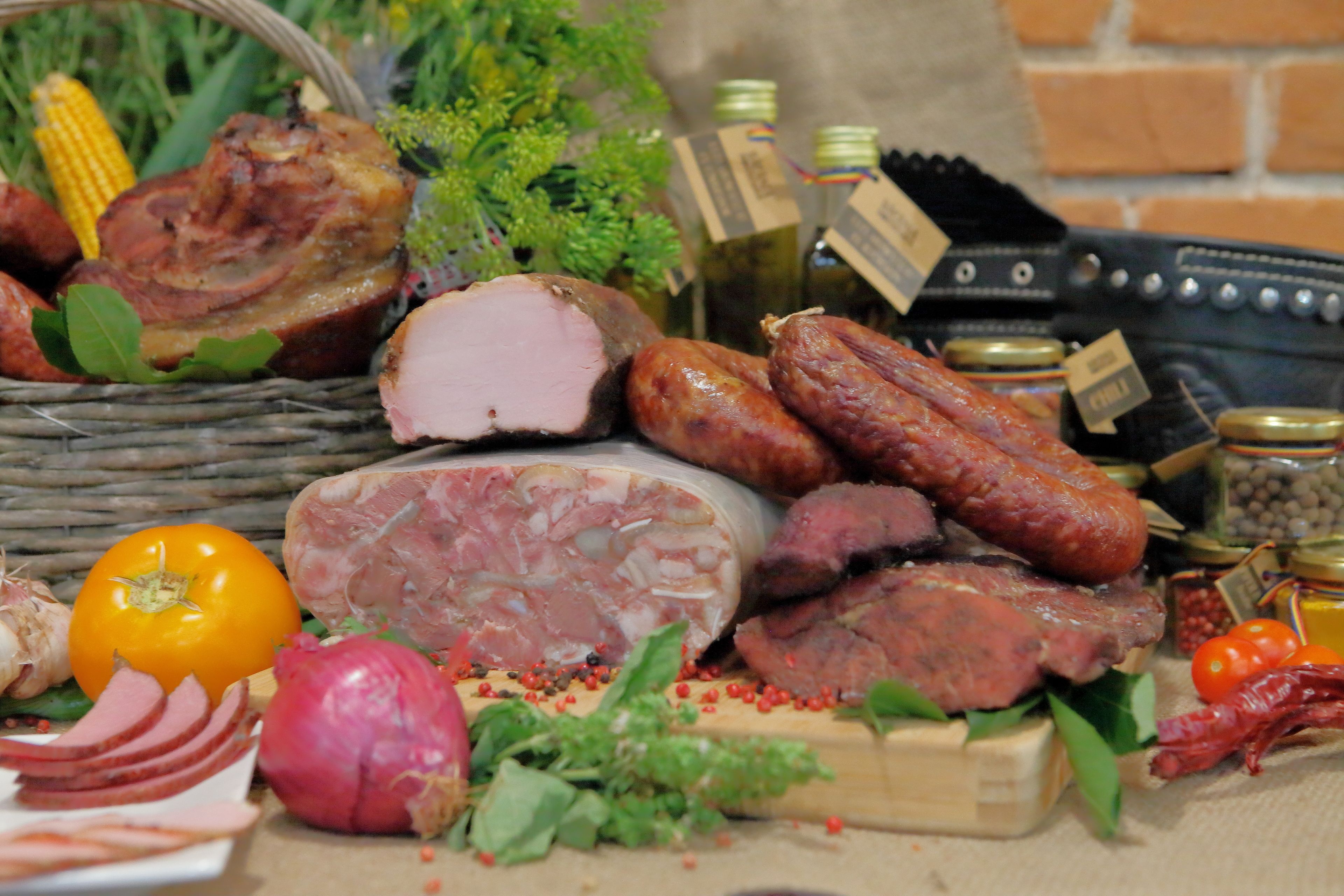 A variety of meats, including sausages, ham, and a large cut of meat, along with some vegetables and condiments.
