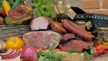 A variety of meats, including sausages, ham, and a large cut of meat, along with some vegetables and condiments.