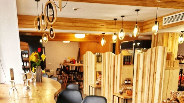 Un comedor moderno con mesas y sillas de madera, una planta en maceta al frente e iluminación colgante.