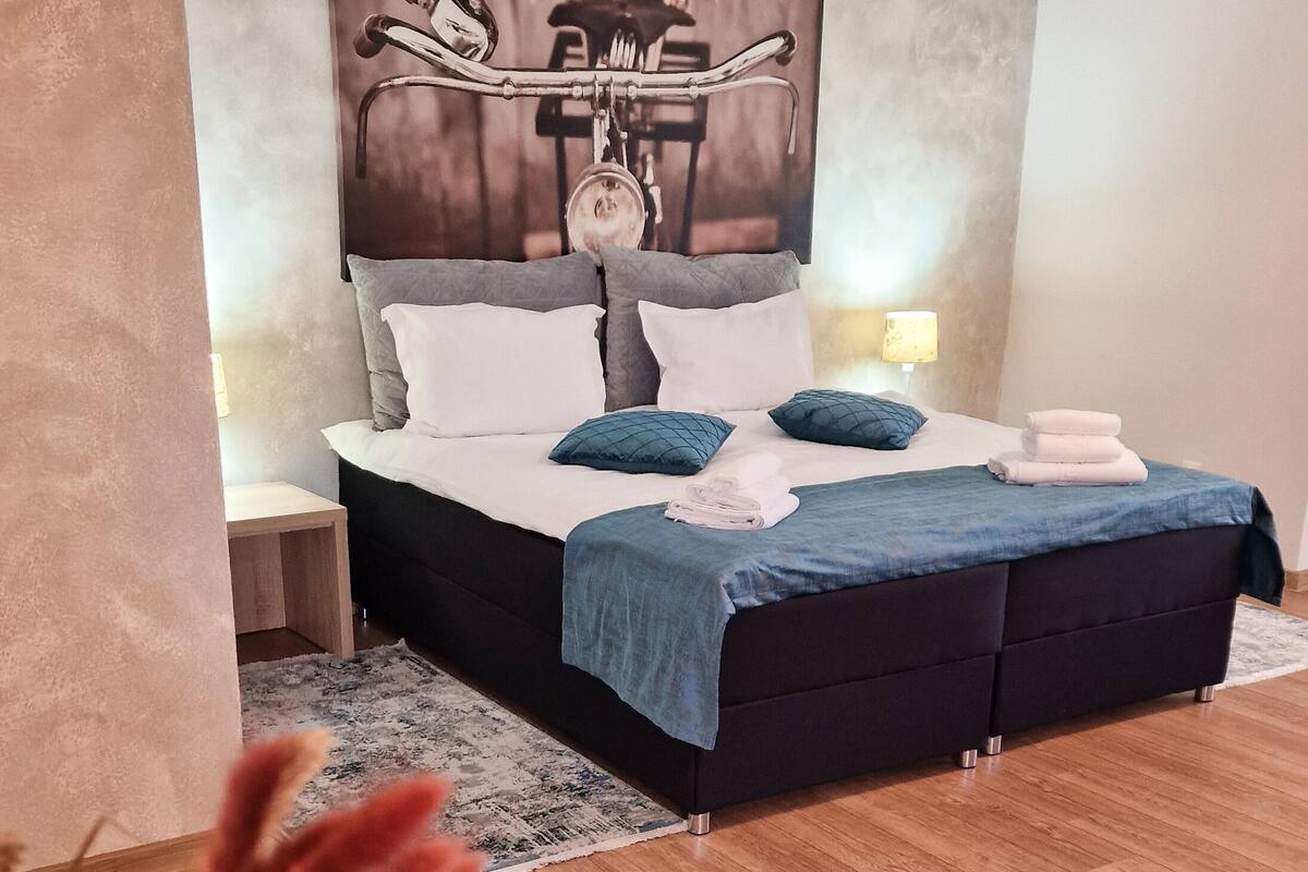 Un dormitori amb llit, taules de nit, obra d'art penjada a la paret i un paviment de fusta.