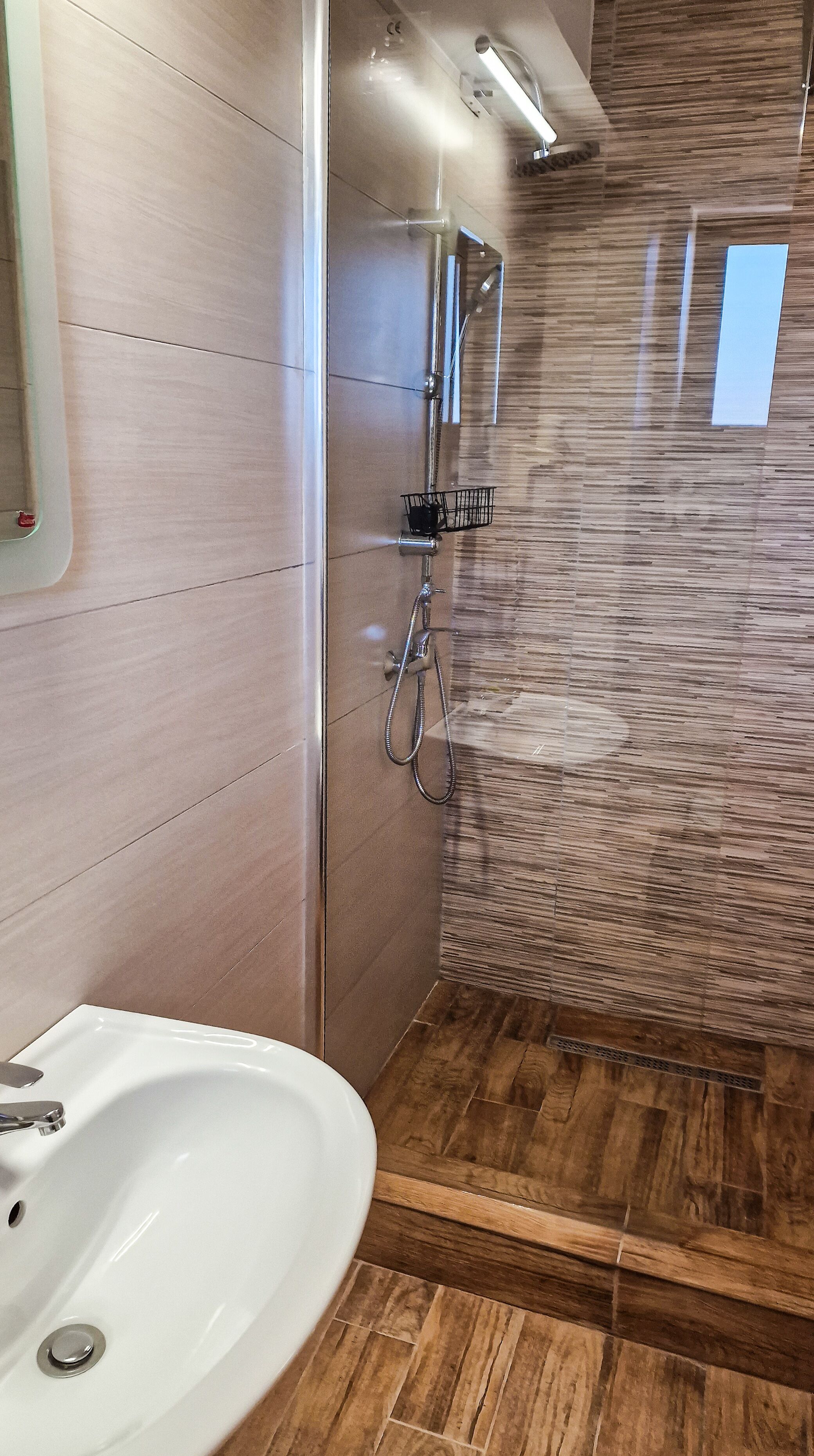 A bathroom with a white sink, a shower with a handheld showerhead, and a wooden wall panel.