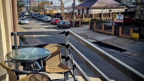 Un balcón con sillones de mimbre y una mesita, con vista a una calle con coches y edificios.