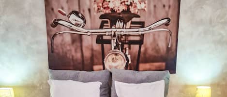 Una cama doble con dos almohadas, una colcha azul y toallas dobladas. Hay dos mesitas de noche con lámparas.