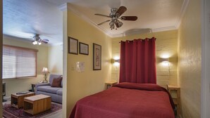 Ein Schlafzimmer mit einem Bett, einem Deckenventilator, einem roten Vorhang und einem kleinen Tisch mit einer Lampe.