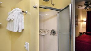 Ein Badezimmer mit Duschkabine aus Glas, einem Handtuchhalter mit weißen Handtüchern, einem Toilettenpapierhalter und einem sichtbaren Duschkopf.