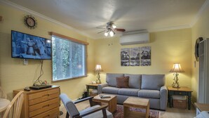 Ein Wohnzimmer mit einer Couch, Sesseln, einem Couchtisch, einem Fernseher und einem Deckenventilator.