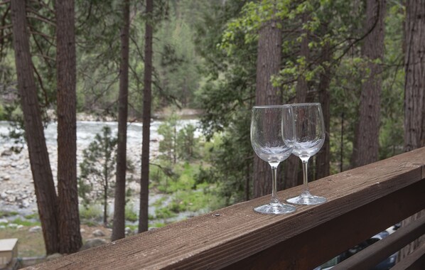 Two empty wine glasses on a wooden railing overlooking a river and forest.