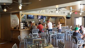 A restaurant with multiple tables and chairs, a bar area, ceiling fans, and televisions on the walls.