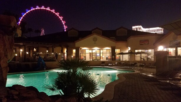A hotel with a swimming pool, a Ferris wheel in the background, and outdoor seating areas.