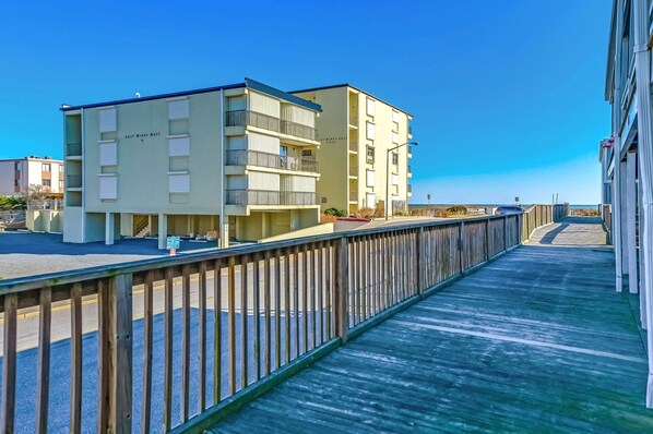 A multi-story building with balconies and a wooden boardwalk leading to it. - Come Stay at this Awesome Home, featured on HGTV's Beachfront Bargain Hunts (Ocean City)