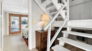 Una escalera que conduce a un piso superior, un aparador de madera, una lámpara y vistas a un balcón con barandilla.
