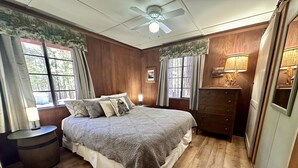 Quarto com cama grande, piso de madeira, ventilador de teto e cômoda com abajur.
