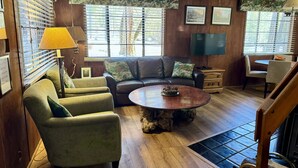 Uma sala de estar acolhedora com sofá, poltronas, mesa de centro e televisão.