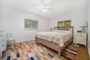 A bedroom with a bed, a dresser, a nightstand, a ceiling fan, and two windows. - The Red House (Wayne Township)