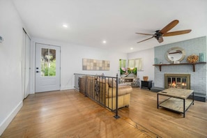 Un salon spacieux doté d’un plancher en bois franc, d’un ventilateur de plafond, d’une cheminée et d’une grande fenêtre.