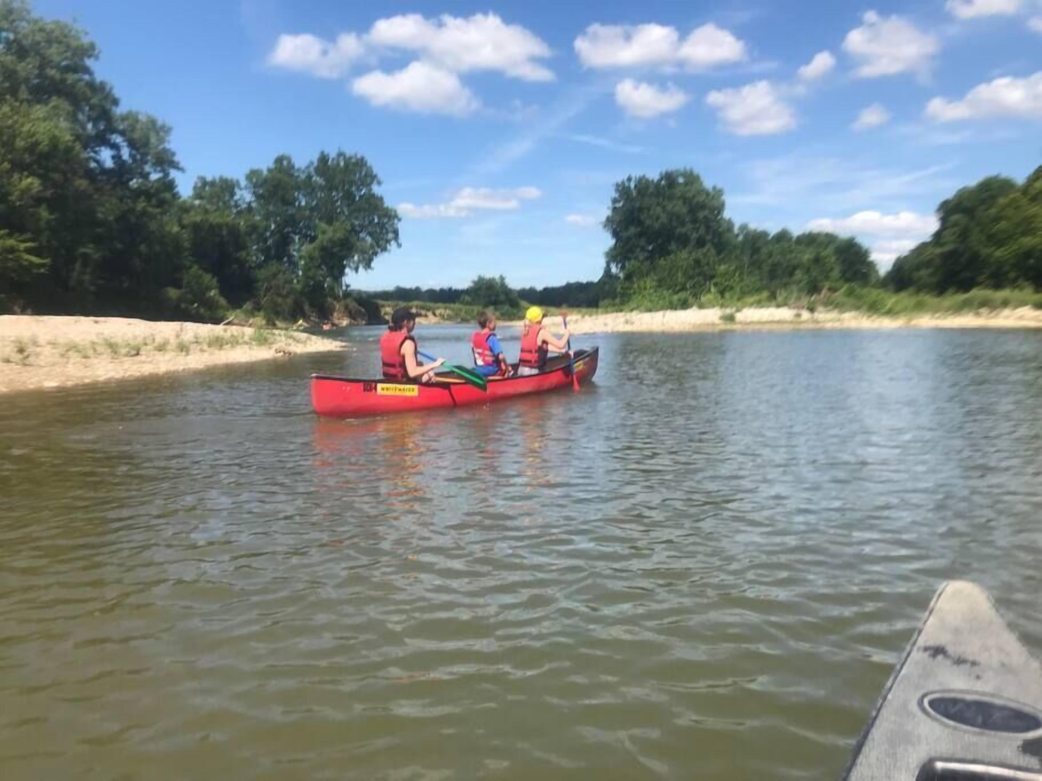 A red canoe with three people paddling on a river.