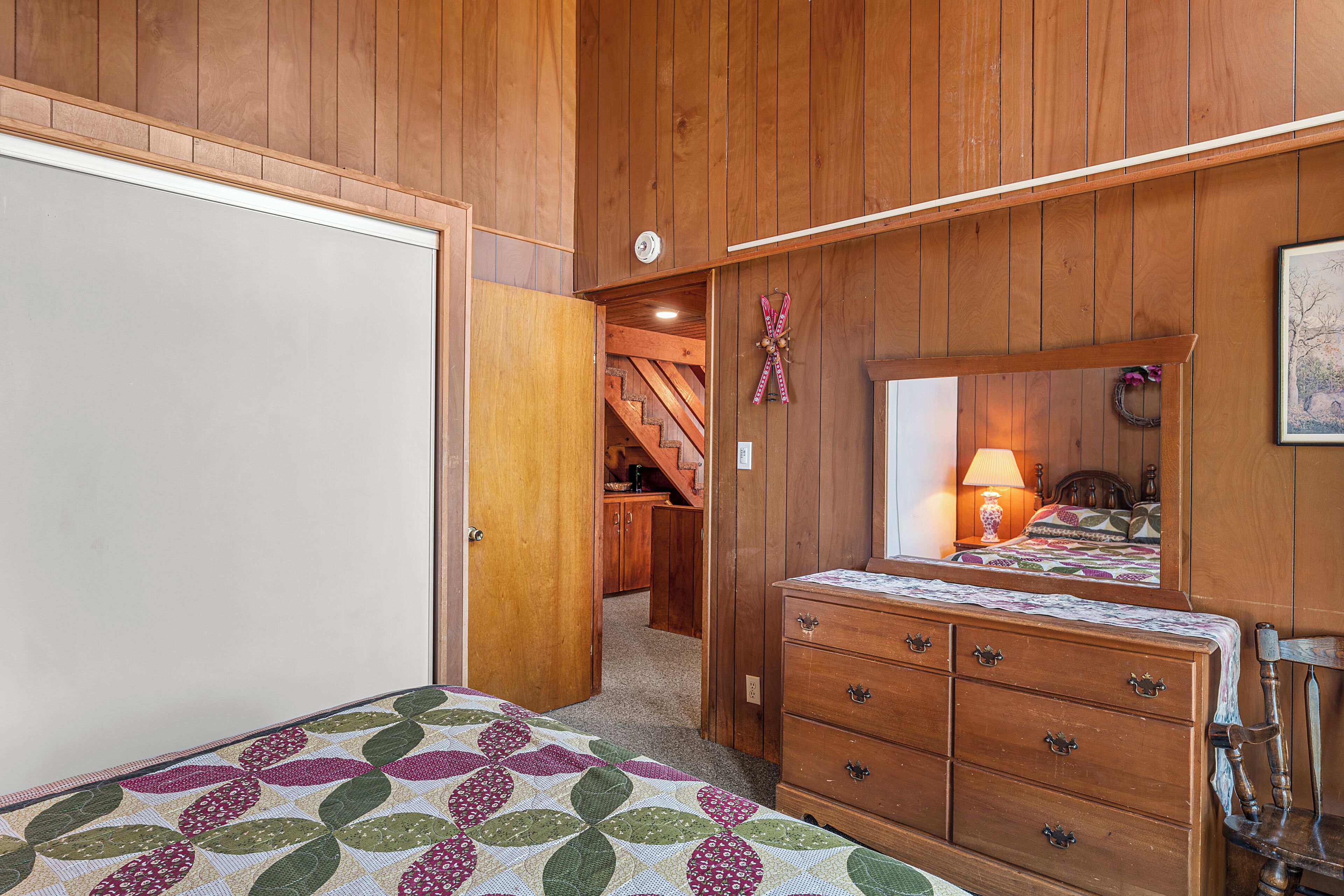 Un dormitorio con paredes de madera, una cama con colcha estampada, un tocador y un espejo.
