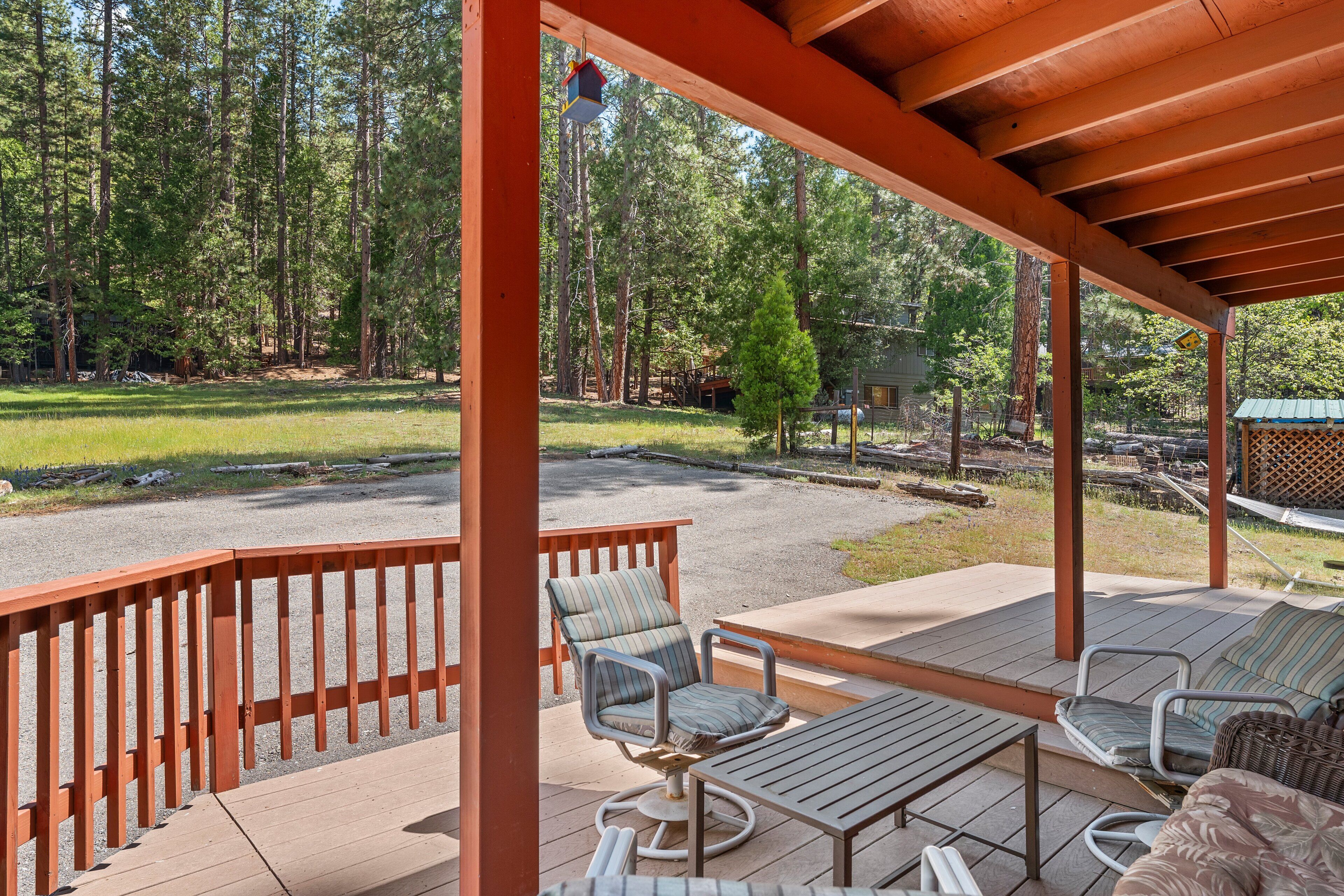 A covered outdoor seating area with a wooden deck, metal chairs, and a table.