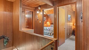 A wooden interior with a staircase, a mirror, and a bedroom visible through an open door.
