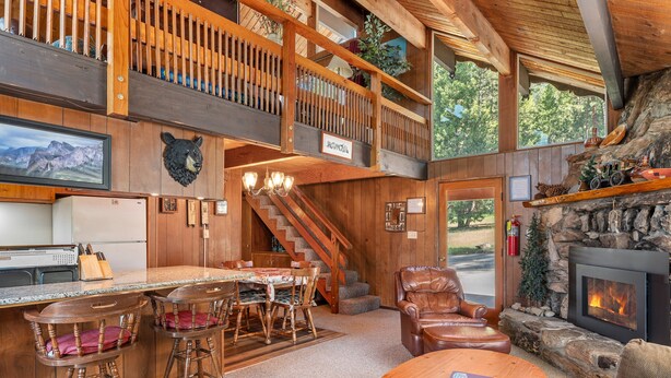 A spacious lodge with a dining area, bar, fireplace, and a staircase leading to a loft.