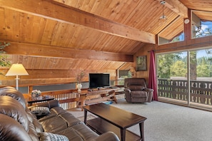 Relax in a warm and inviting living area with a high ceiling, comfortable sofa, and stunning forest views.