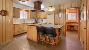 A kitchen with wooden cabinets, a central island with stools, a stove, and a refrigerator.