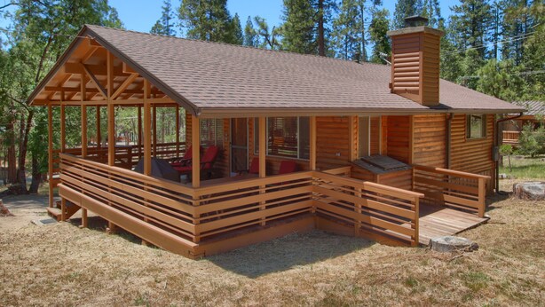 A wooden cabin with a porch, a chimney, and a covered deck area.