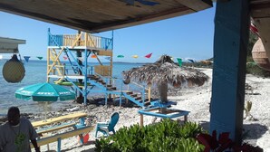 Een gebouw aan het strand met een trap, een rieten dak en vlaggen in verschillende kleuren.