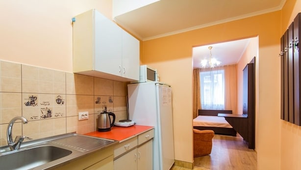 A compact kitchen with a sink, cabinets, and a microwave. There is a small dining area with a table and chairs. - 1 Bedroom Apartment on Sq. Staryi Rynok 1 (Lviv)