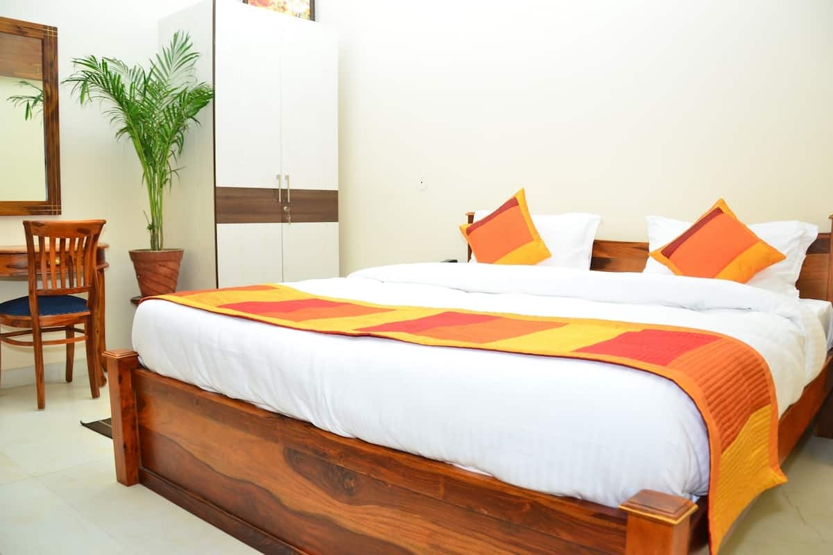A neatly made bed with a wooden headboard, a desk with a chair, and a potted plant.