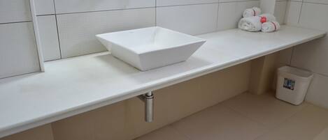 A modern bathroom with a white sink, a towel rack, and a trash bin.