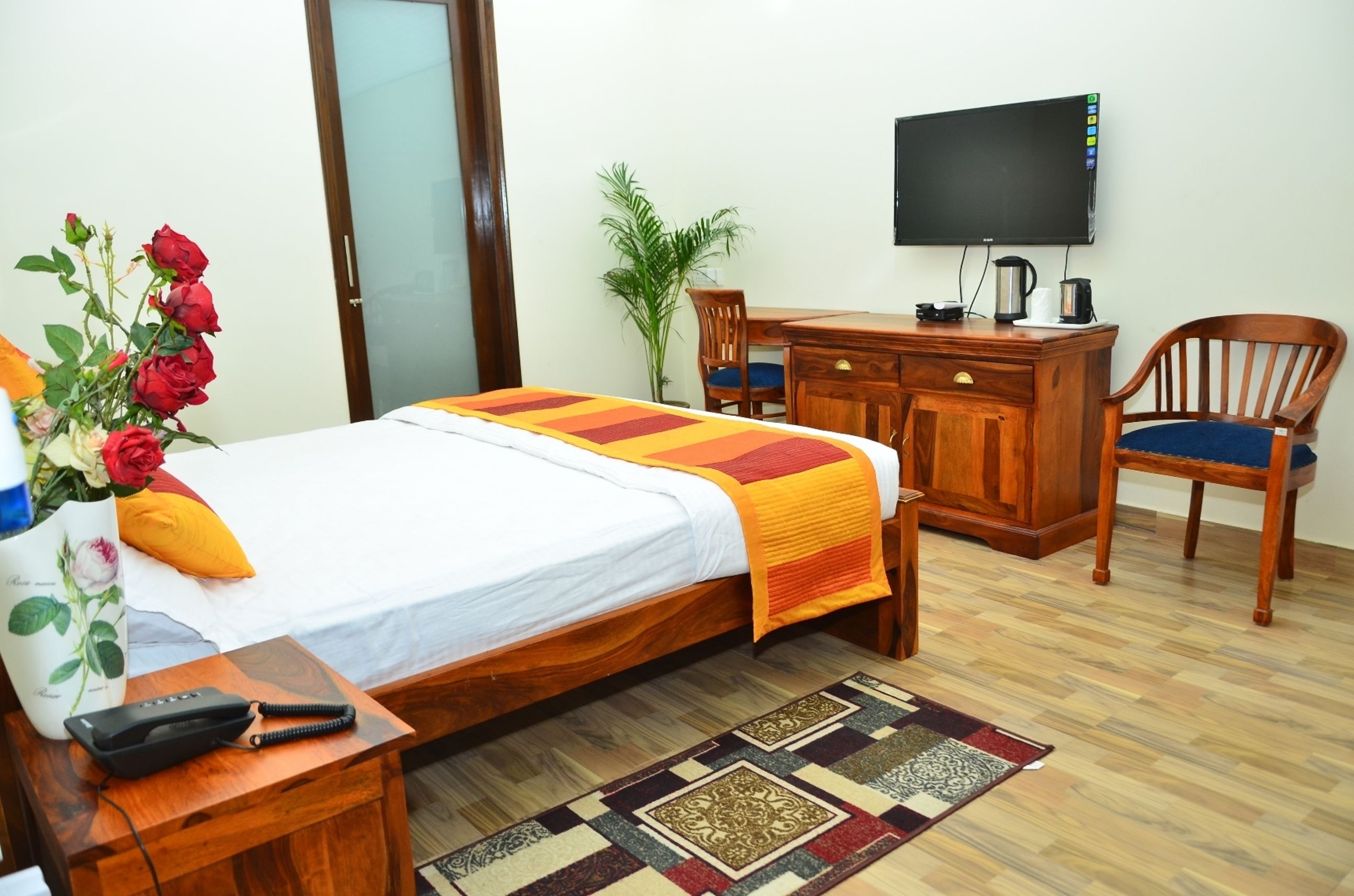 Quarto de hotel com cama, escrivaninha, cadeira, televisão e planta.