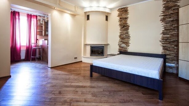 A bedroom with a bed, a fireplace, wooden flooring, and a stone accent wall. - 1 Bedroom Apartment Knyazya Leva 2 (Lviv)